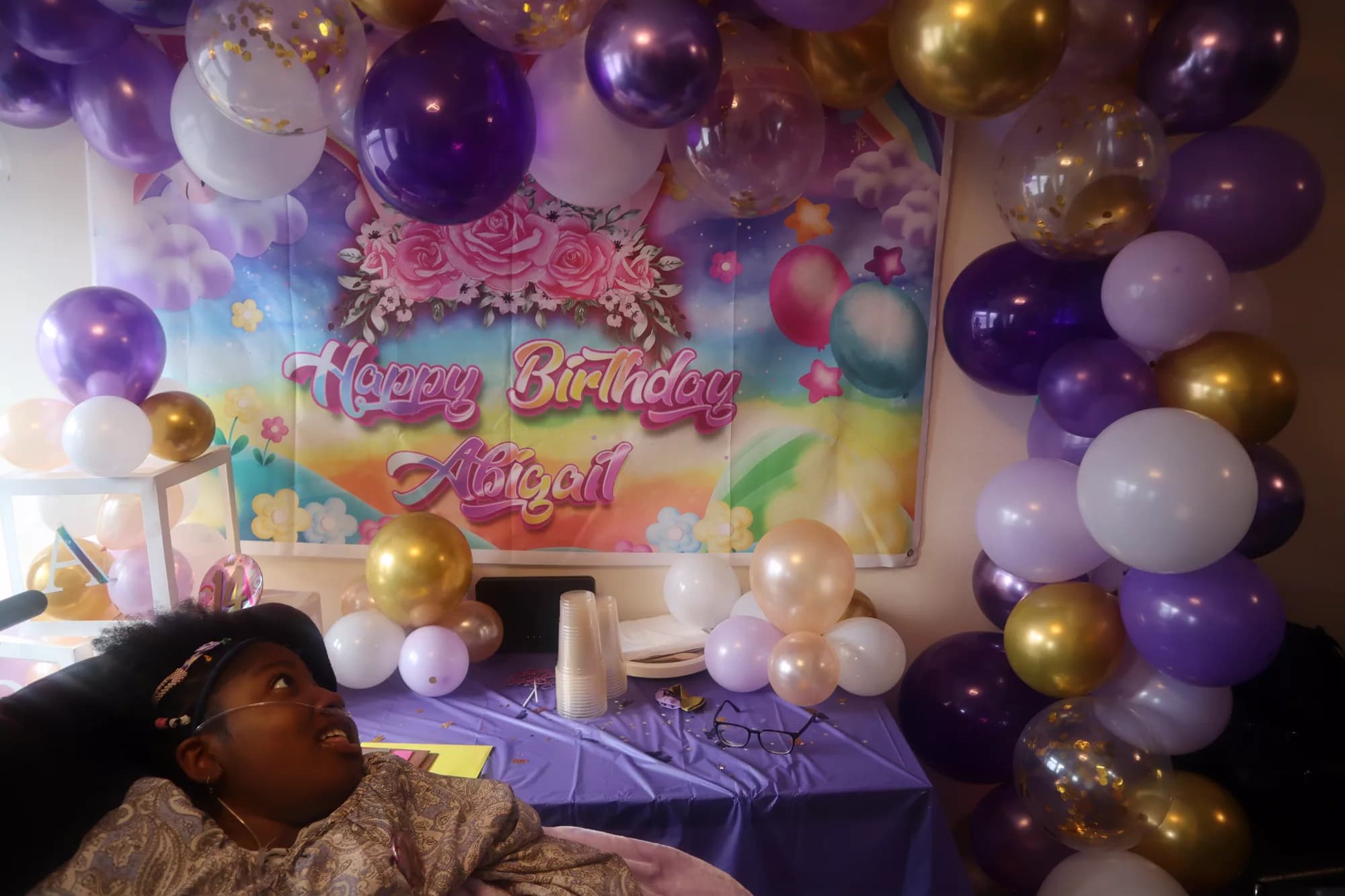 Abigail in front of purple and gold birthday decorations.